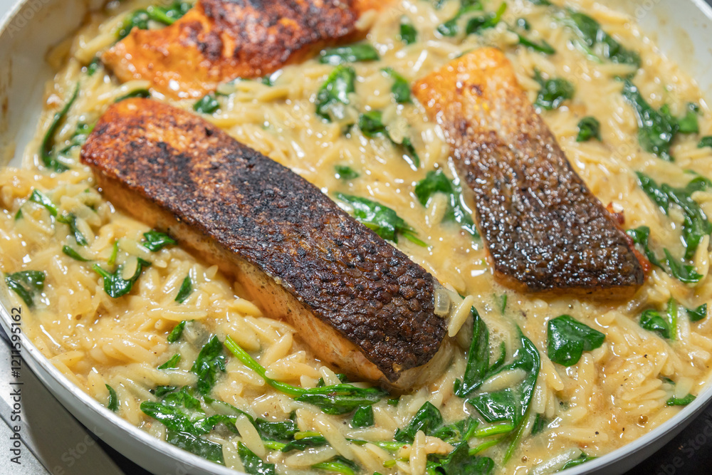 Close-up of a cooked salmon filet with orzo pasta and spinach in a white pan, showcasing a healthy and delicious meal