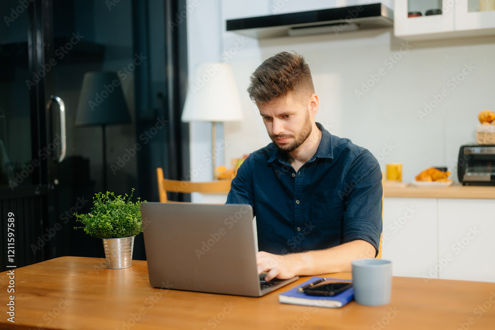 Businessman using laptop while sitting at home. Young man sitting in kitchen and working Businessman using laptop while sitting at home. Young man sitting in kitchen and working