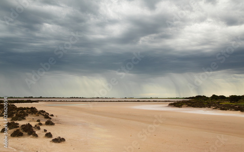 A storm with visible rain falling approaches threateningly towards a dry pink lake which is salty as shown by the sparse salt bush vegetation on the Yorke Peninsula near Stansbury in South Australia. photo