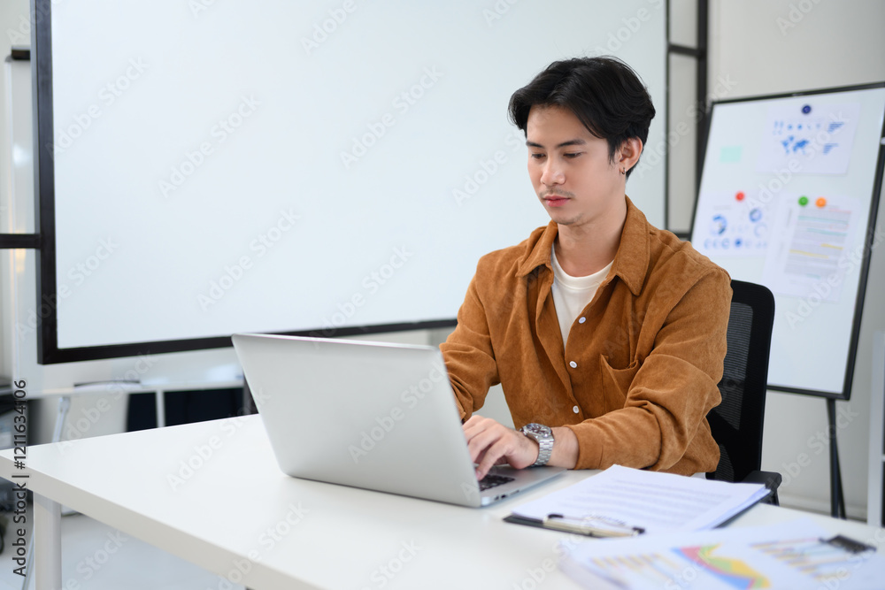 Young businessman focused on working at his laptop in a bright office space Young businessman focused on working at his laptop in a bright office space