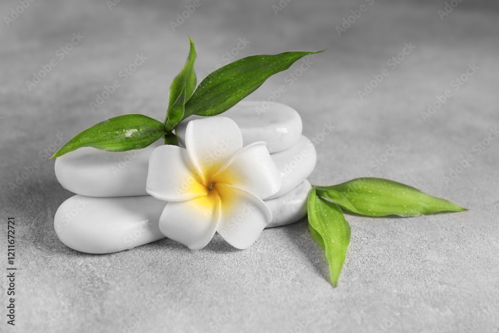 Spa stones, plumeria flower and green leaves on grey table, closeup Spa stones, plumeria flower and green leaves on grey table, closeup