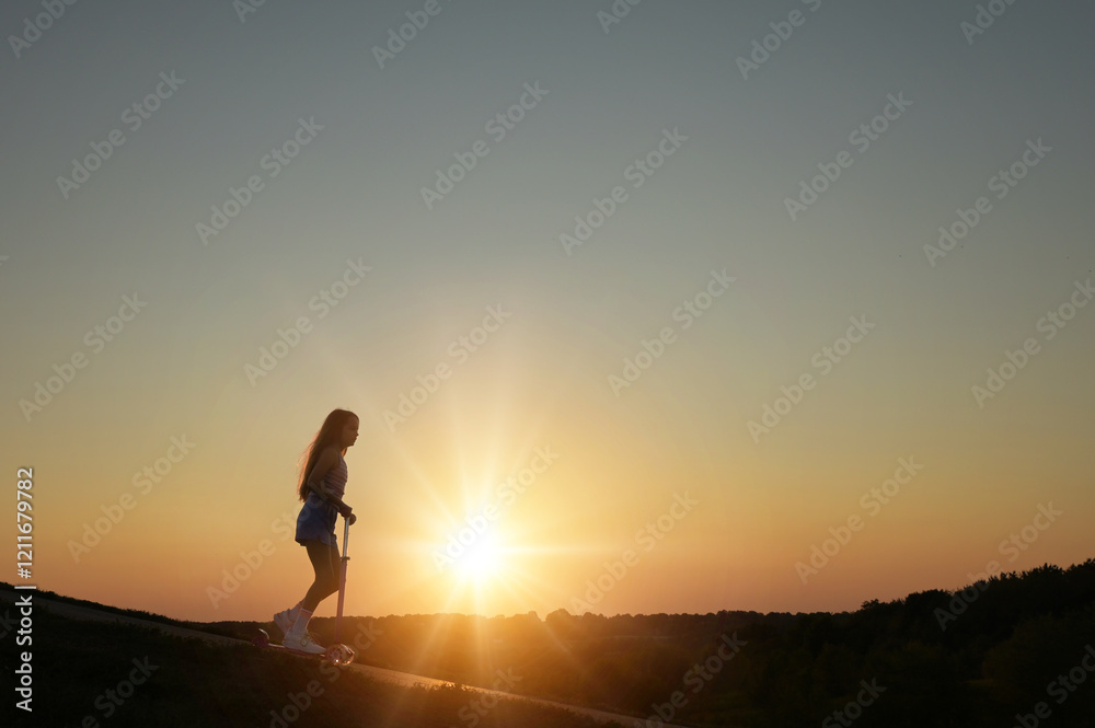 Tween girl riding scooter outdoors at sunset