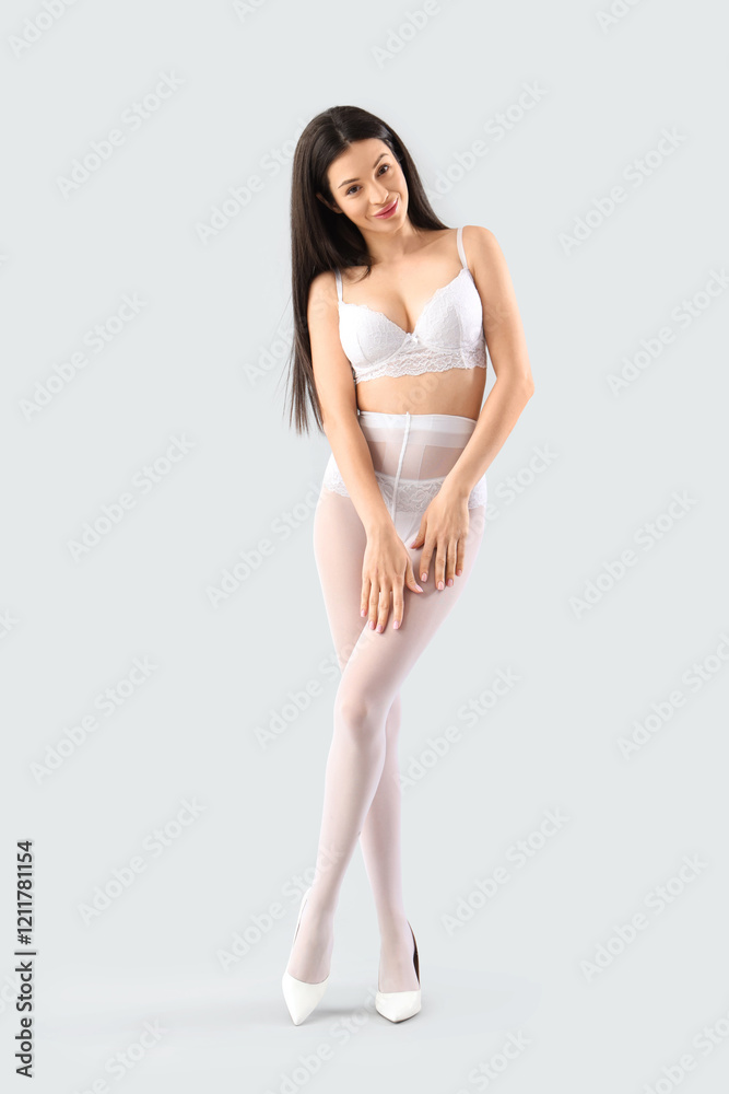 Fototapeta premium Attractive young woman in underwear and white tights on light background