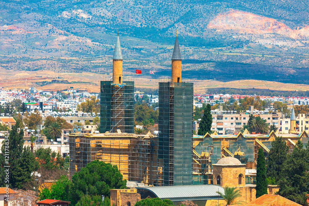 Selimiye Mosque in Nicosia, Cyprus, stands amid urban and mountainous scenery, framed by twin minarets under renovation. Its striking Ottoman architecture reflects rich cultural history of the region