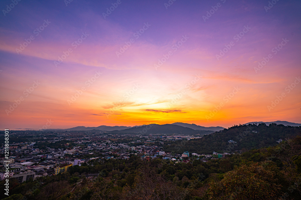 A scenic view of a town nestled among lush green mountains at sunset, with a temple structure perched on the hillside and a vibrant orange sky creating a warm, tranquil atmosphere. A scenic view of a town nestled among lush green mountains at sunset, with a temple structure perched on the hillside and a vibrant orange sky creating a warm, tranquil atmosphere.
