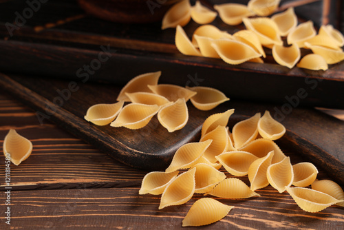 Trays and scattered raw pasta shells on wooden background, closeup photo