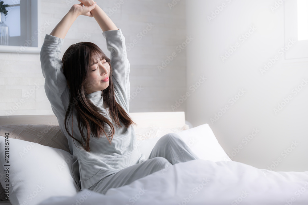 ベッドの上で寝起きで伸びやストレッチをする女性 ベッドの上で寝起きで伸びやストレッチをする女性