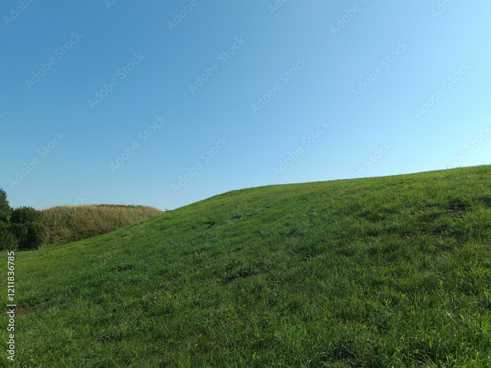 Salduve hill during sunny day. Small hill. Grass is growing on hill. Staircase leading to the top. Sunny day with white and gray clouds in sky. Nature. Salduves piliakalnis. Salduve hill during sunny day. Small hill. Grass is growing on hill. Staircase leading to the top. Sunny day with white and gray clouds in sky. Nature. Salduves piliakalnis.