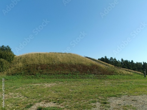 Salduve hill during sunny day. Small hill. Grass is growing on hill. Staircase leading to the top. Sunny day with white and gray clouds in sky. Nature. Salduves piliakalnis. photo