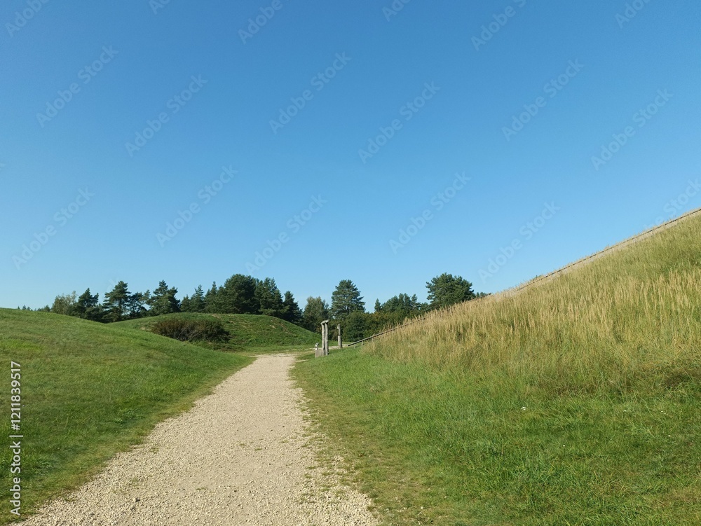 Salduve hill during sunny day. Small hill. Grass is growing on hill. Staircase leading to the top. Sunny day with white and gray clouds in sky. Nature. Salduves piliakalnis. Salduve hill during sunny day. Small hill. Grass is growing on hill. Staircase leading to the top. Sunny day with white and gray clouds in sky. Nature. Salduves piliakalnis.