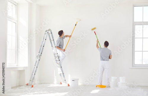 Fototapeta Naklejka Na Ścianę i Meble -  Two male painters in uniform paint a wall white with a roller. Home repair concept. Professional work of builders. Modern apartment renovation, living room interior decoration