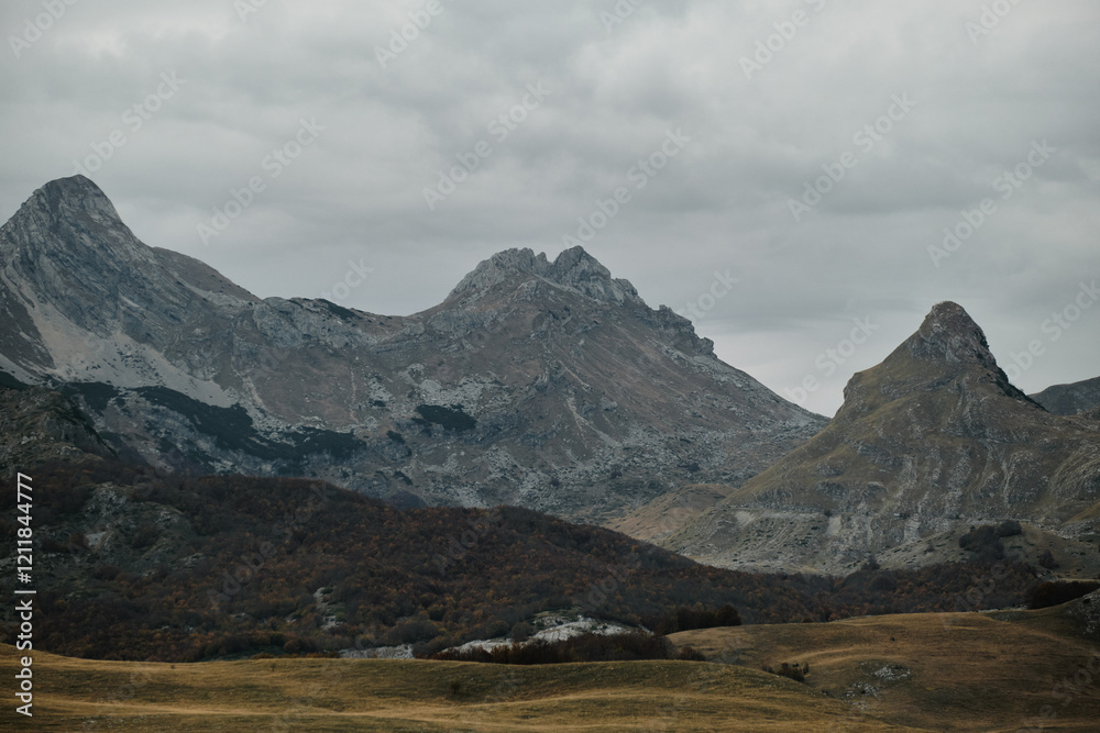 Mountain landscape in Durmitor National Park, Montenegro country in autumn season on cloudy day. Pointed rocky mountain ranges and endless fields with dry yellow grass in the valley. Mountain landscape in Durmitor National Park, Montenegro country in autumn season on cloudy day. Pointed rocky mountain ranges and endless fields with dry yellow grass in the valley.