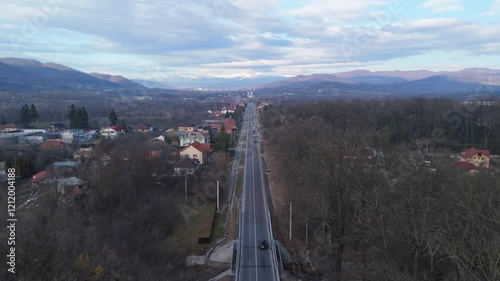 A small village road with houses, trees, and distant mountains, aerial view photo