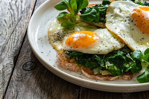 Canvas-taulu Crispy toast with stewed spinach and fried eggs with runny yolks on wooden table