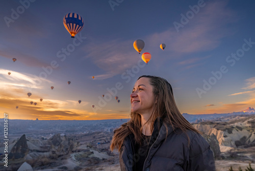 Obraz na płótnie A cute girl close up playfully smiling and posing against the backdrop of floating hot air balloons in Cappadocia during winter w salonie