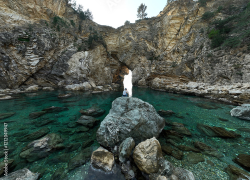 Obraz na płótnie Girl sitting on a rock with her back to the camera, looking at the channel and rock arch in Kings Bay lagoon with turquoise Mediterranean water w salonie