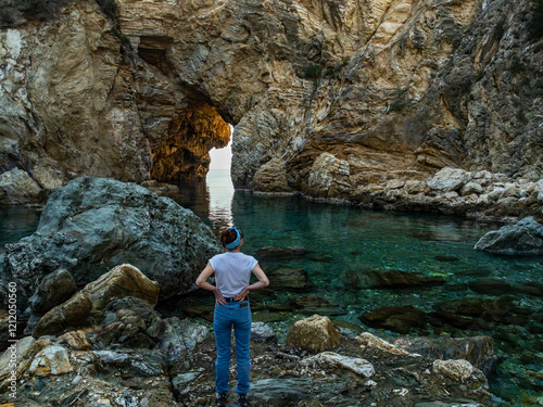 Girl standing with her back in a white t-shirt and jeans, hands on hips, looking up at Kings Bay lagoon with a rock arch photo