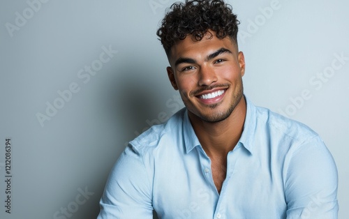 A relaxed full-figured man with short curly hair and a gentle smile, wearing a light blue button-up shirt, posed on a clean white surface