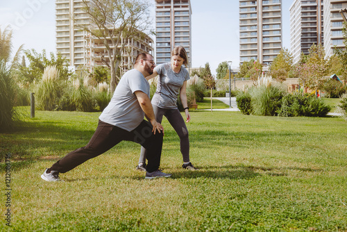 Man with extra weight doing work-up in public park with his trainer.  photo