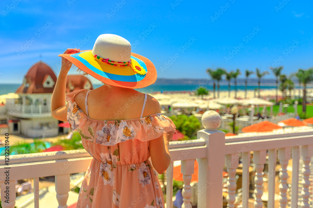 Tourist woman in hat at a balcony looking scenic arial view of West Coast in Pacific Ocean, Coronado Island, San Diego. Luxury hotel on blurred background. Summer in California, USA.