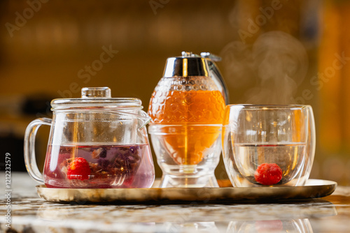 Forest fruits tea. Beautiful plate deco made of a glass pot with boiled water, a double glass with tea and honey in background. Steams coming out of hot tea glass. photo