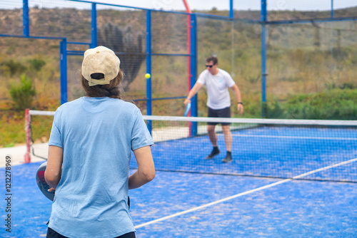 Obraz na płótnie A woman standing with her back to the camera, poised and ready to return the ball on an outdoor padel court, w salonie