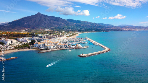 aerial view of luxury yachts in Puerto Banús marina, habor wall and the lighthouse Faro Puerto Banús, prominent Pico de la Concha mountain behind, Marbella, Malaga, Costa del Sol, Spain