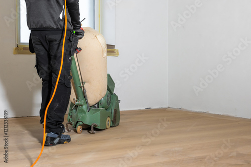 Schilderij op canvas A worker operates a green floor polishing machine on a light wooden floor in a white walled room with taped windows, indicating ongoing renovations