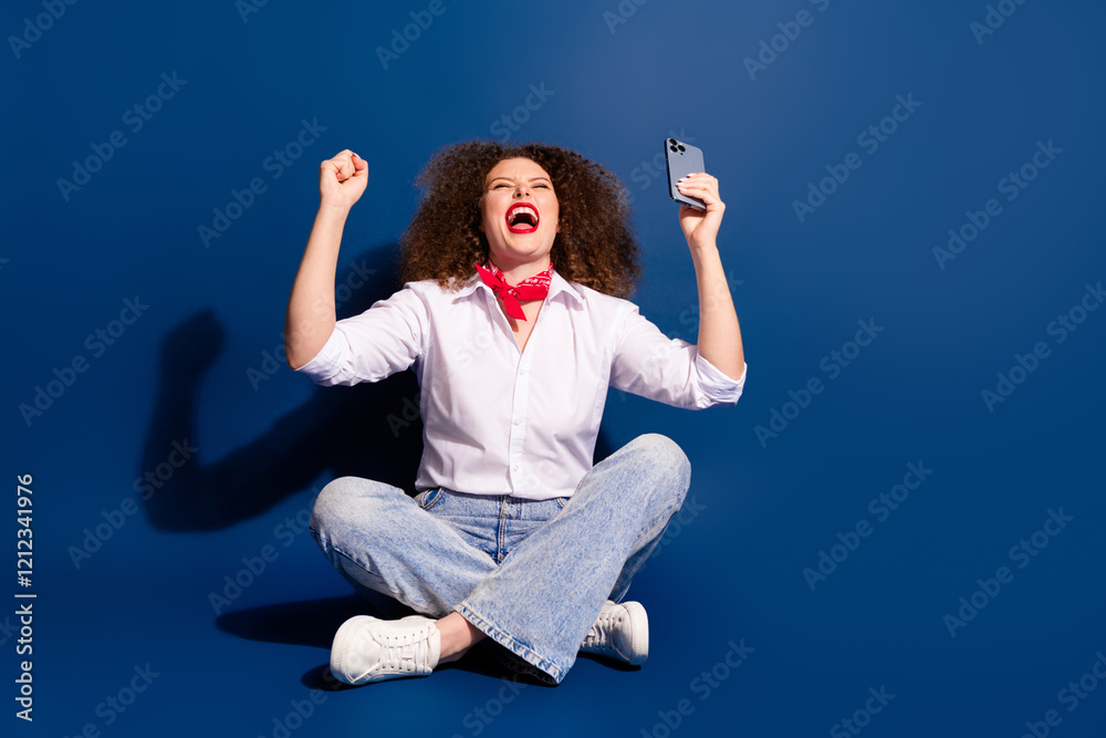 Full length photo of cheerful lucky lady dressed white shirt winning game modern gadget empty space isolated blue color background Full length photo of cheerful lucky lady dressed white shirt winning game modern gadget empty space isolated blue color background