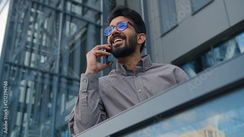 Joyful Indian man talking mobile phone on office terrace outdoors happy smiling Arabian businessman employer ceo executive talk smartphone in city friendly business conversation cellphone call outside photo