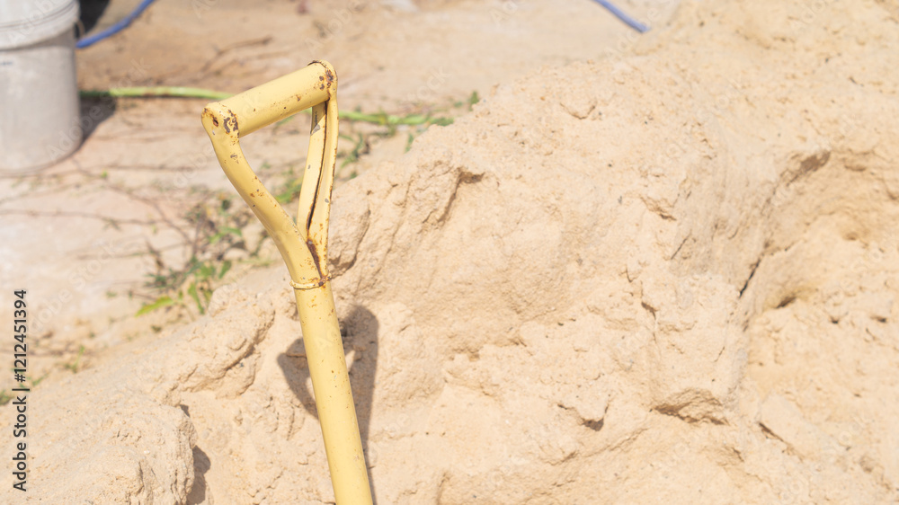 Closeup of yellow shovel handle on background of pile of rough sand. Equipment for construction work and space for text Closeup of yellow shovel handle on background of pile of rough sand. Equipment for construction work and space for text