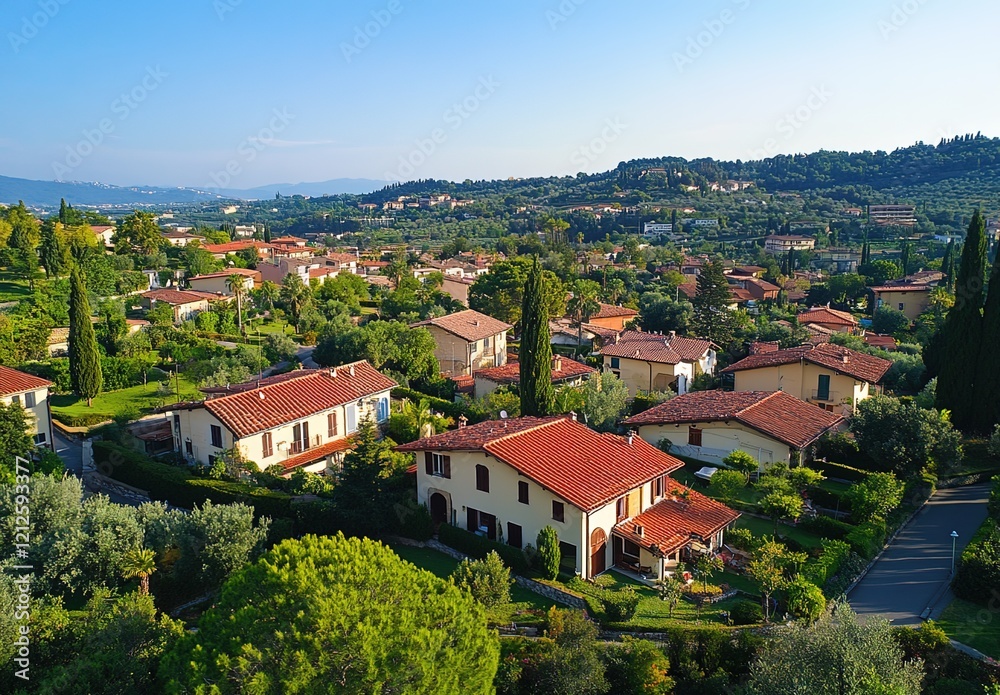 Obraz premium Aerial view of a residential area in Italy, where there is a row with many houses and green trees between them. The buildings have red roof tiles