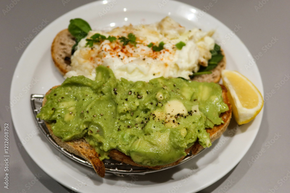 Two slice of sourdough bread toastwith avocado paste with black pepper and egg white crab meat on another slice. Lemon slice on the side on a white plate Two slice of sourdough bread toastwith avocado paste with black pepper and egg white crab meat on another slice. Lemon slice on the side on a white plate