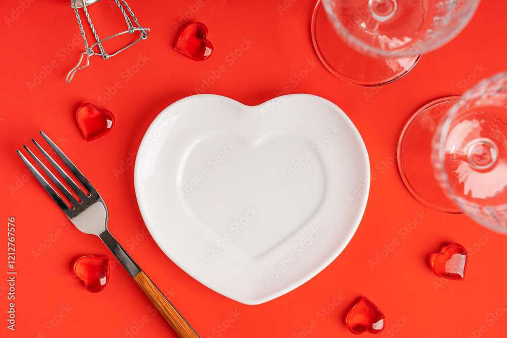 Top view of bright red table served for celebration of party or romantic engagement dinner with white empty ceramic heart shaped plate, flute wine glasses, fork and festive holiday decoration Top view of bright red table served for celebration of party or romantic engagement dinner with white empty ceramic heart shaped plate, flute wine glasses, fork and festive holiday decoration