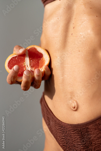 Close-Up of a Woman's Toned Midsection Holding a Grapefruit Half in a Brown Bikini photo