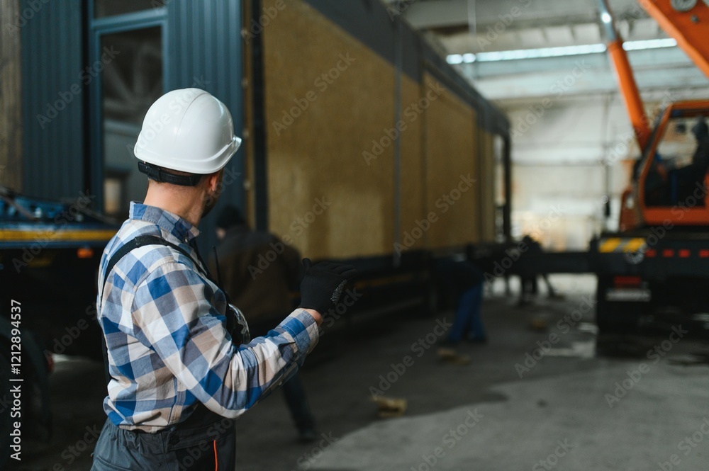 A worker controls the process of loading a modular house onto a truck. Transportation and delivery concept A worker controls the process of loading a modular house onto a truck. Transportation and delivery concept