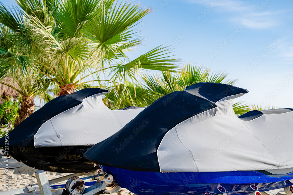 Two jet skis on the shore covered with a protective cover. Preparation for rest, start of racing and sailing.