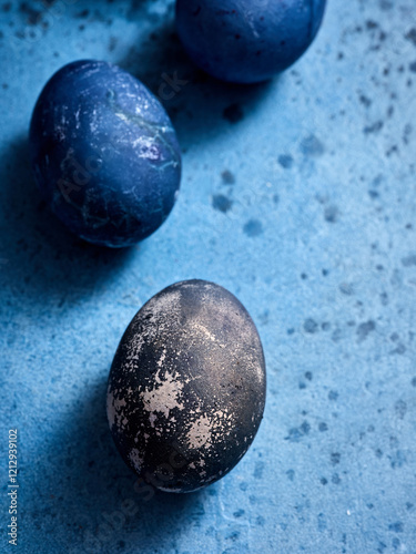Delicate dark and blue Easter eggs rest on a textured blue surface, showcasing intricate patterns and celebrating the arrival of spring festivities