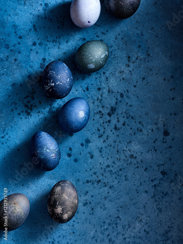 Various handcrafted decorative eggs in shades of blue, green, and black are artfully arranged on a rich blue surface. The vibrant colors create a festive atmosphere perfect for spring celebrations photo