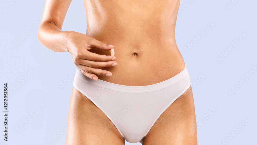 Closeup cropped view of young unrecognizable woman in white panties holding pink pill near her nude belly. Diet supplement or contraception concept, healthcare medicine treatment, studio banner Closeup cropped view of young unrecognizable woman in white panties holding pink pill near her nude belly. Diet supplement or contraception concept, healthcare medicine treatment, studio banner