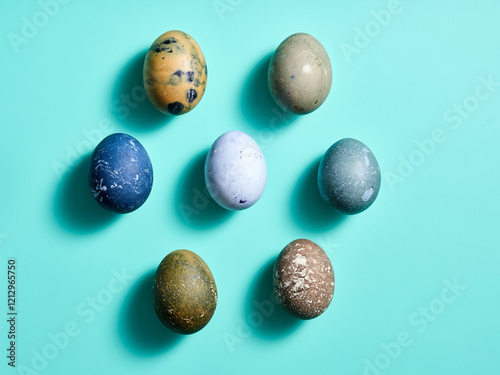 Various uniquely decorated Easter eggs in shades of blue, green, and brown are skillfully arranged on a vibrant turquoise surface, showcasing their elaborate designs photo