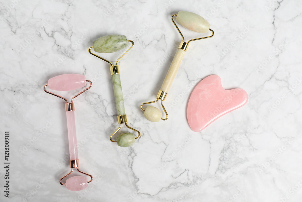 Face rollers and gua sha tool on white marble background, flat lay Face rollers and gua sha tool on white marble background, flat lay