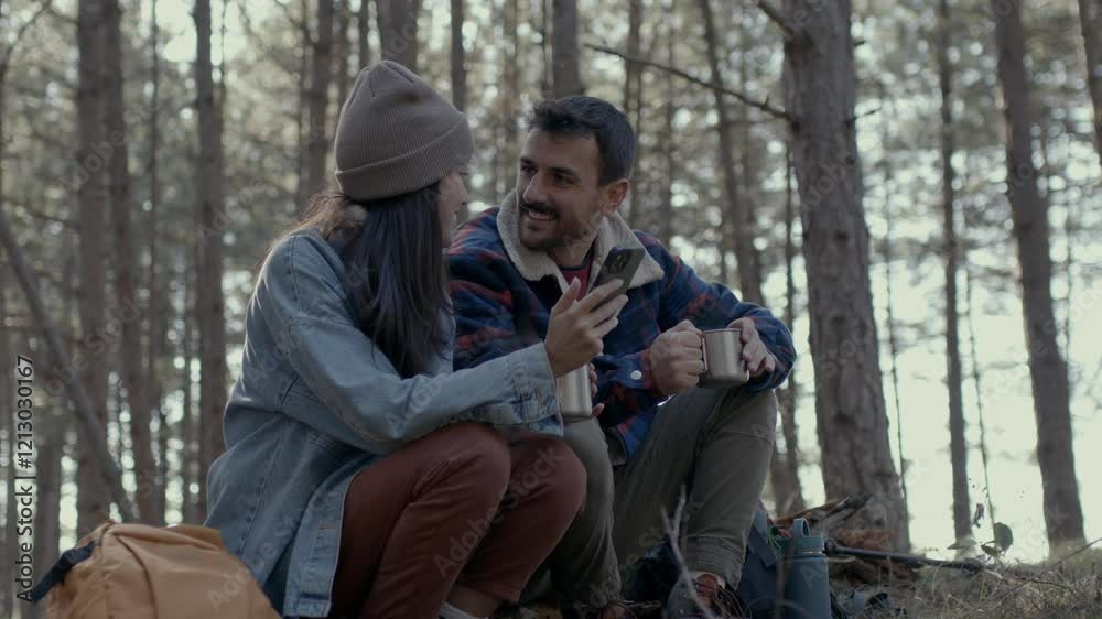 Hikers sitting on a log in the woods, sharing a moment with coffee and a smartphone Hikers sitting on a log in the woods, sharing a moment with coffee and a smartphone