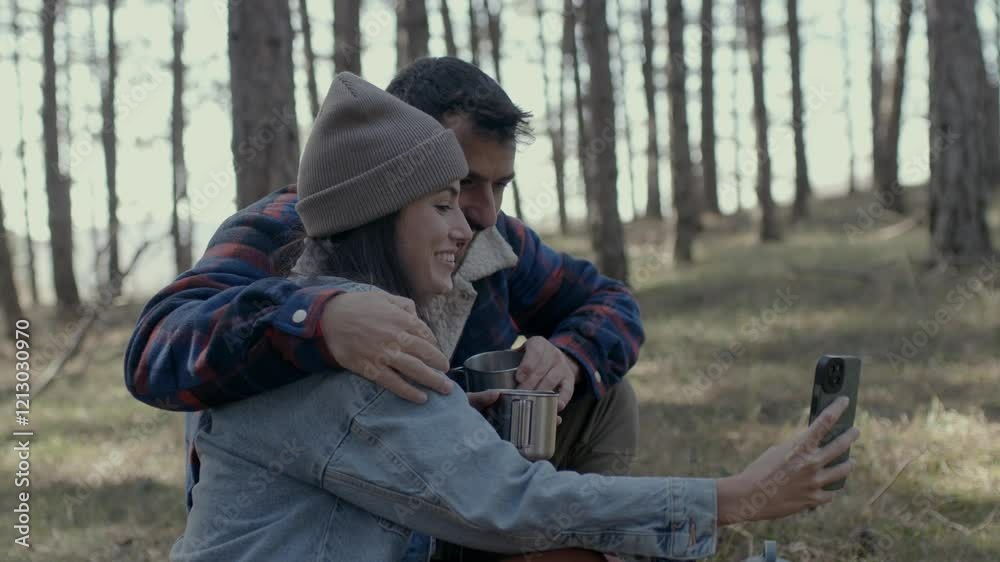 Hikers sitting on a log in the woods, sharing a moment with coffee and a smartphone Hikers sitting on a log in the woods, sharing a moment with coffee and a smartphone