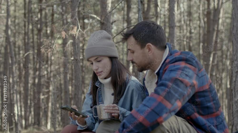 Man and woman resting on a forest trail, sipping hot beverages and checking a smartphone together. 4k video Man and woman resting on a forest trail, sipping hot beverages and checking a smartphone together. 4k video
