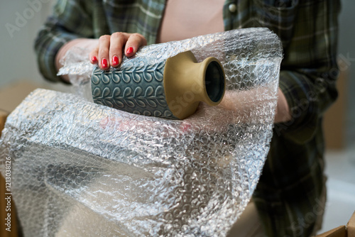 Fotografie Hand of unrecognizable young woman wrapping vase into bubble wrap before packing