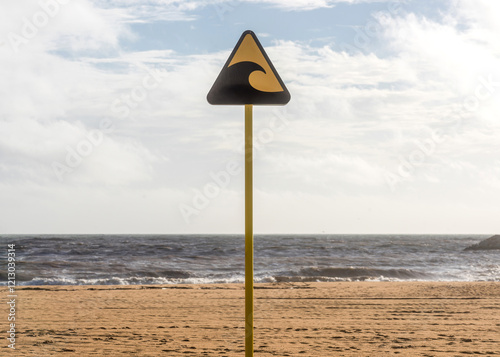 Tsunami warning sign standing on beach with ocean waves in background during cloudy weather photo