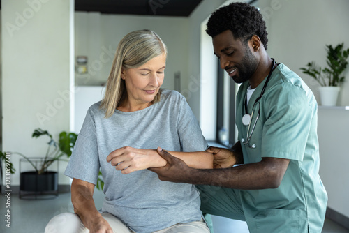 African American male doctor hand doing physical therapy by extending elbow of mature female patient photo