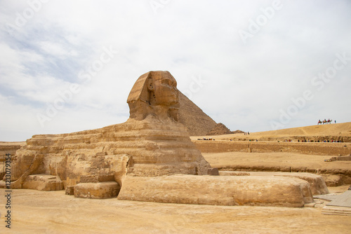 Historically known statue called Sfinx with face of human, body of lion and Cheop's pyramid in the background.