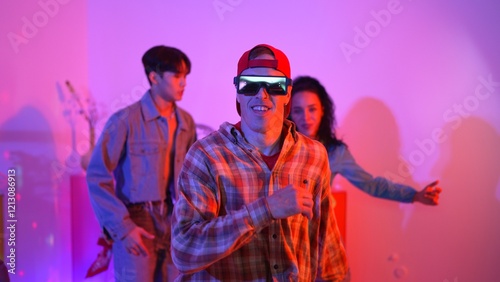 Diverse happy people moving to lively music with neon light at studio. Attractive hipster dancing while asian man show energetic movement while multicultural team cheering and supporting. Regalement. photo